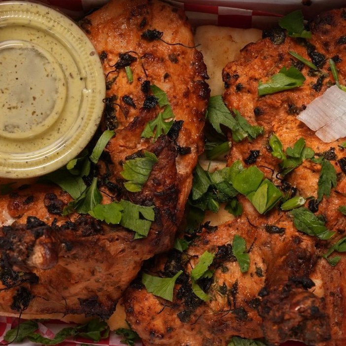 Charred tandoori chicken with coriander beside a bowl of sauce